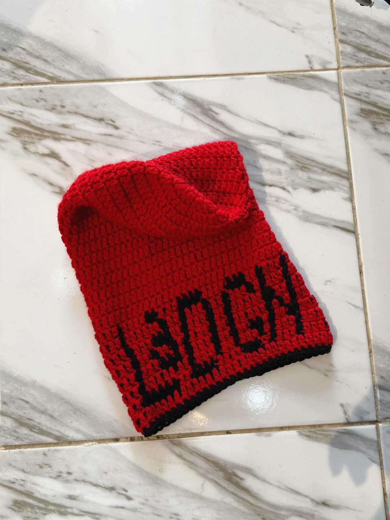 Pièce Invention personnalisée en crochet rouge, prénom crocheté dans la maille, posée sur marbre