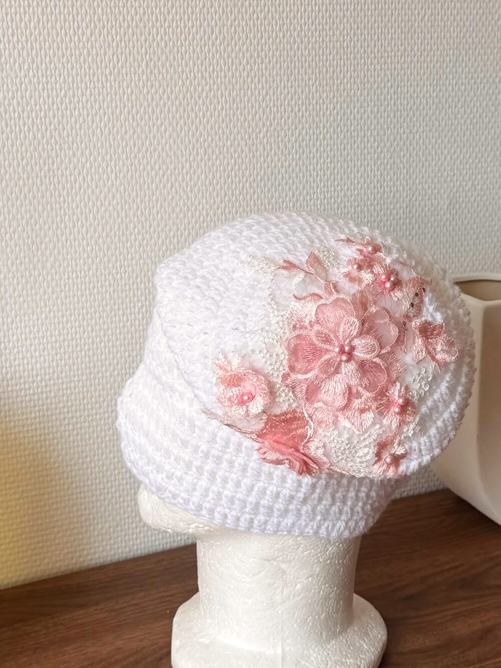 Bonnet Gina Bloom — crochet blanc à fleurs roses brodées et perles, sur tête mannequin en lumière du jour