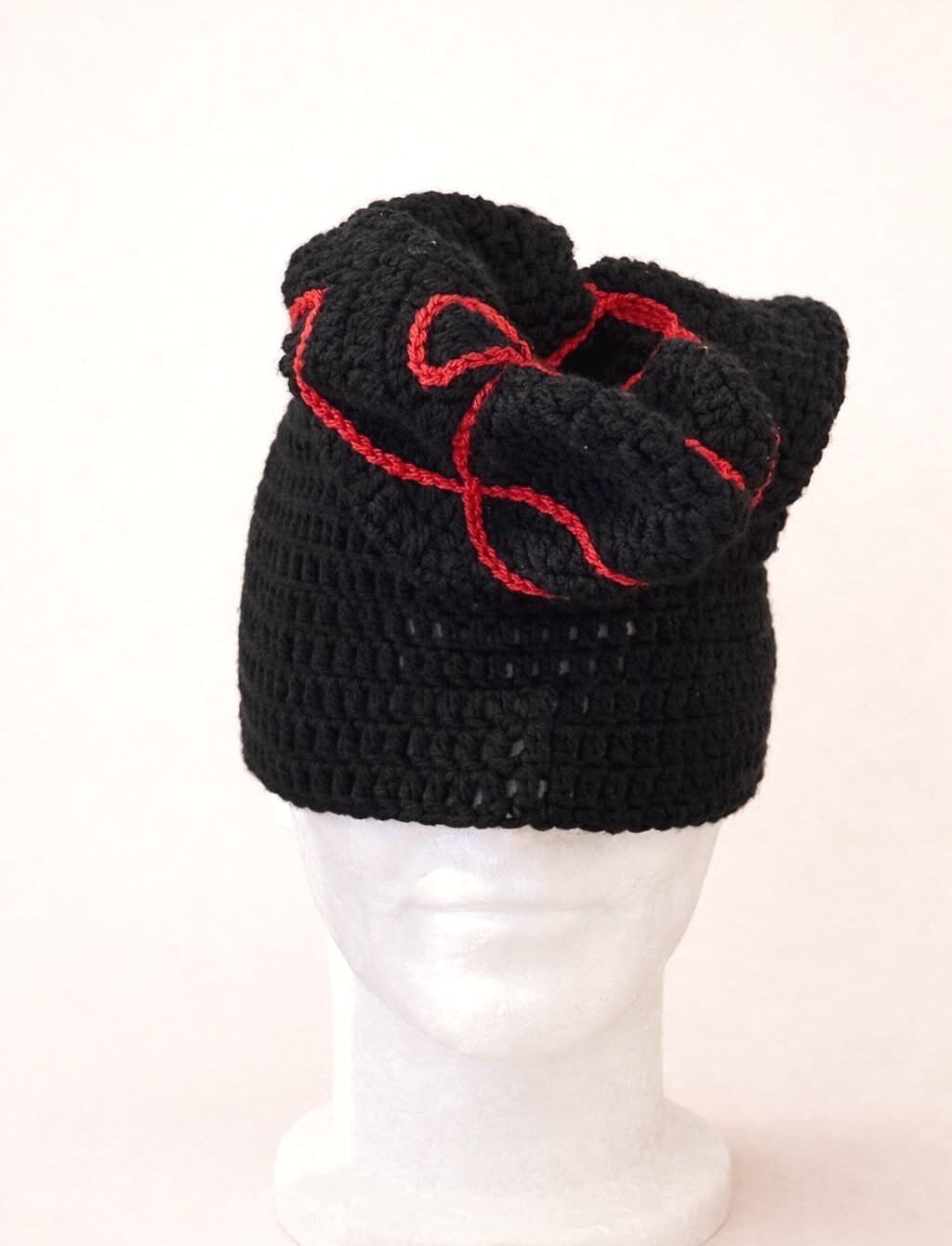 Bonnet Invention — pièce noire sculpturale à volutes rouges, sur tête mannequin, fond clair