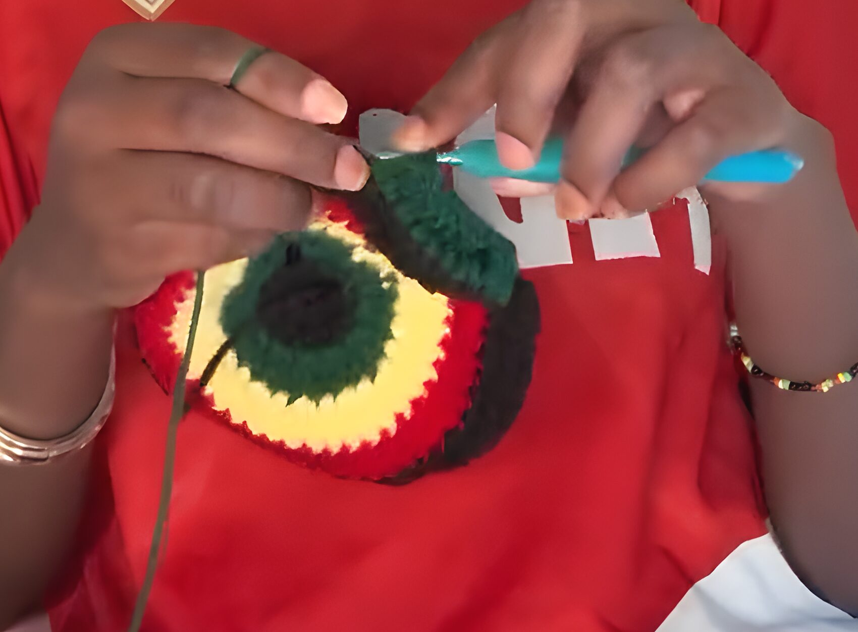 Gros plan des mains et du crochet turquoise formant un disque au motif rasta