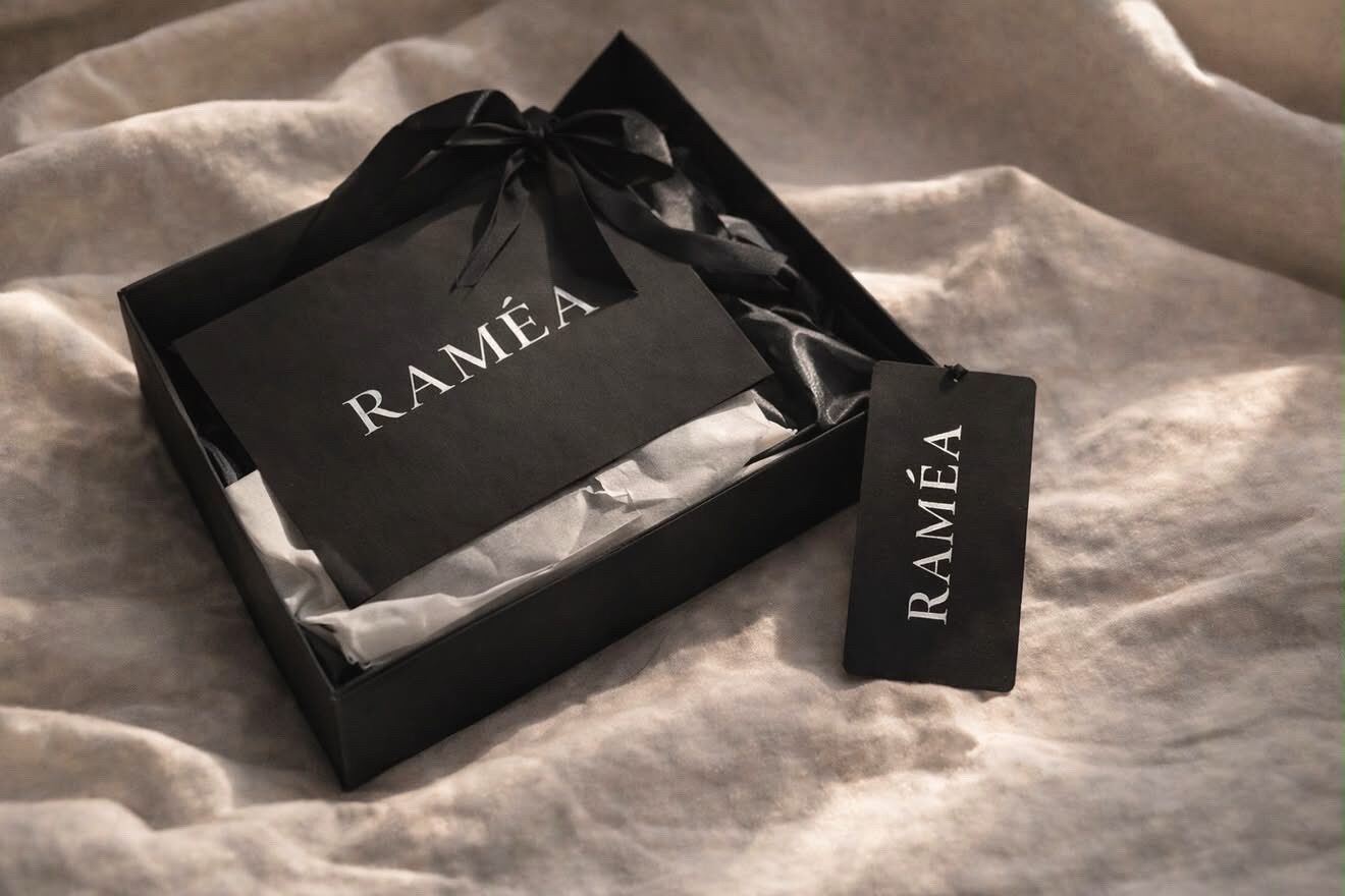 Coffret cadeau RAMÉA noir, noué d'un ruban et de son étiquette, posé sur un drap de lin ivoire
