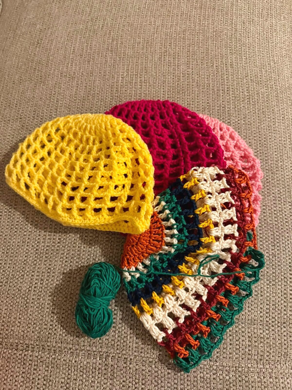 Plusieurs bonnets RAMÉA en crochet ajouré — jaune, framboise, vert et crème — disposés sur une toile de lin