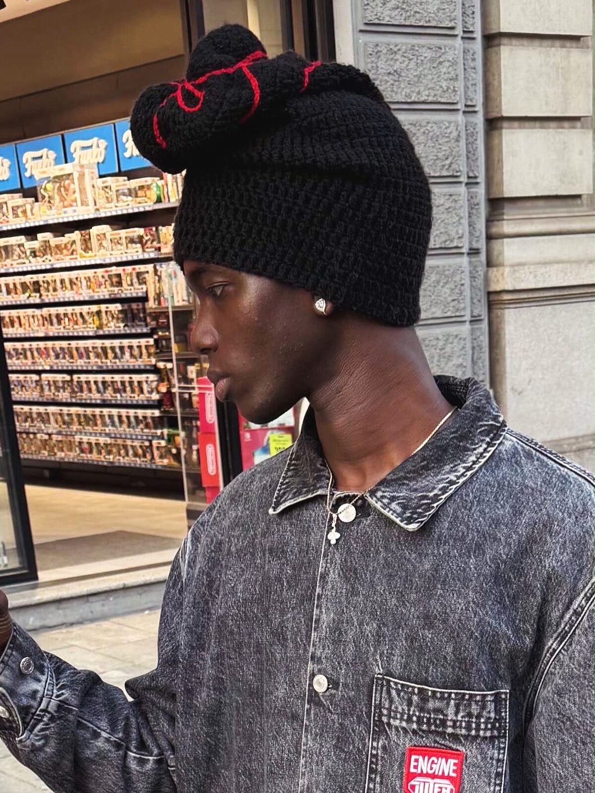 Bonnet Invention noir à volutes rouges, porté de profil avec une veste en jean dans la rue